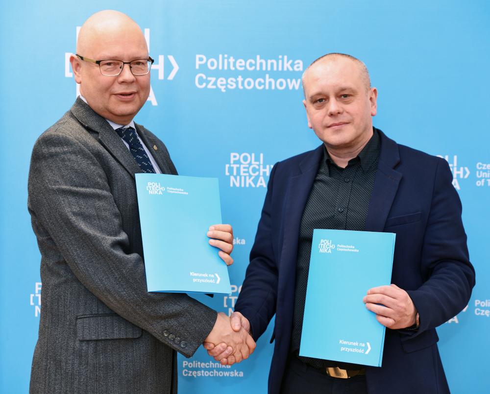 Na zdjęciu Piotr Urbaniak - Dyrektor Powiatowego Urzędu Pracy w Częstochowie oraz dr hab. inż. Rafał Kobyłecki, prof. Politechniki Częstochowskiej - Prorektor ds. rozwoju w strojach biznesowych stoją naprzeciw siebie i ściskają dłonie na tle niebieskiej ścianki z logo Politechniki Częstochowskiej. W drugiej ręce trzymają zamknięte, niebieskie teczki z dokumentami. Uścisk dłoni symbolizuje zawarcie porozumienia i rozpoczęcie współpracy między podmiotami.